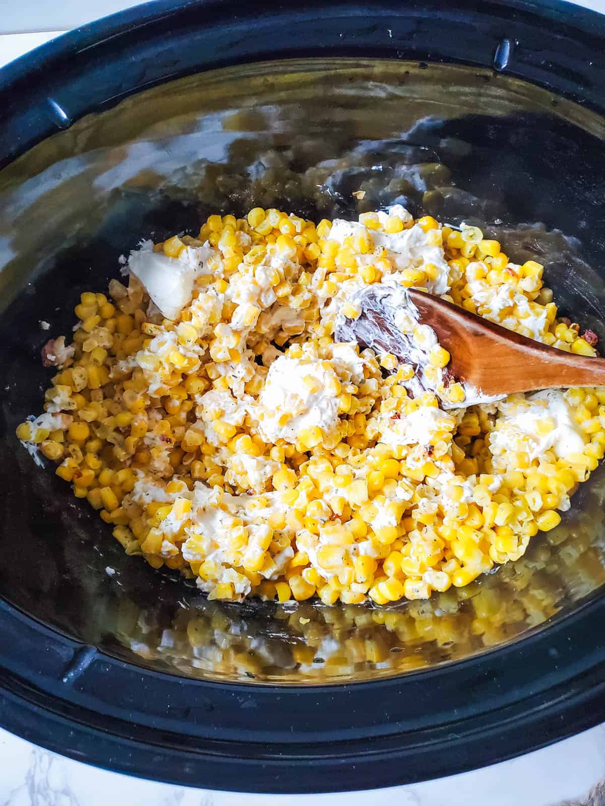 A crockpot with a spoon stirring creamy corn with cream cheese.