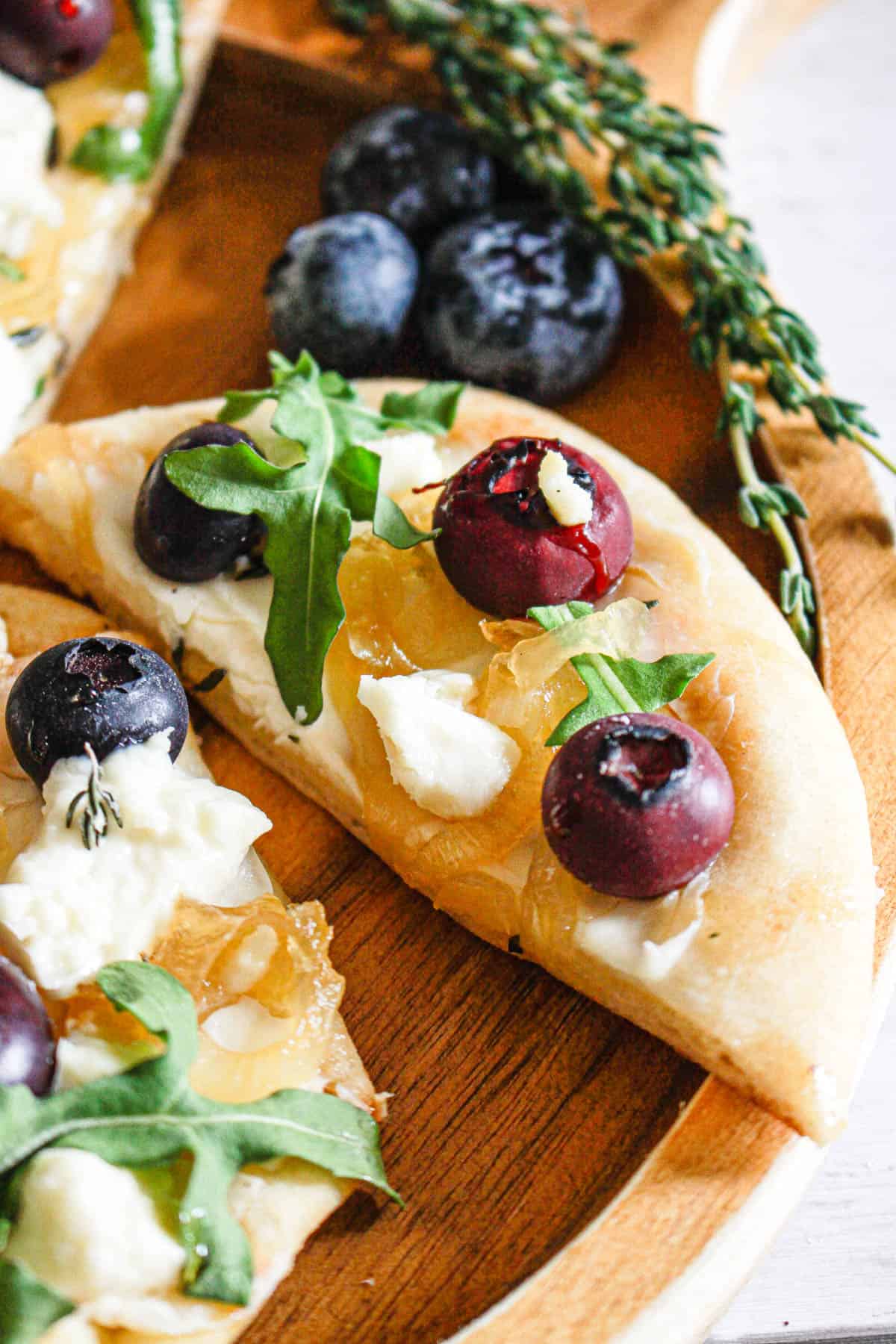 Easy flatbread recipe with blueberries, goat cheese, honey, cream cheese, onions, and fresh thyme, and arugula.