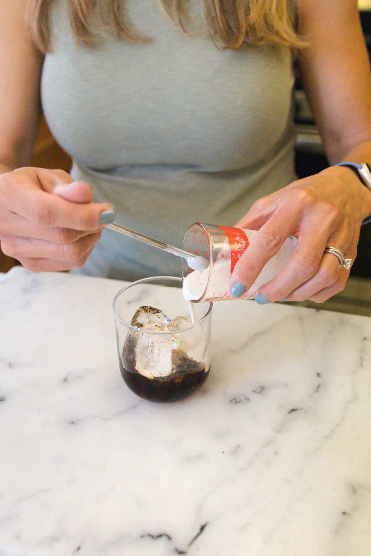 Woman pouring cream over a glass of Kahlua and ice.