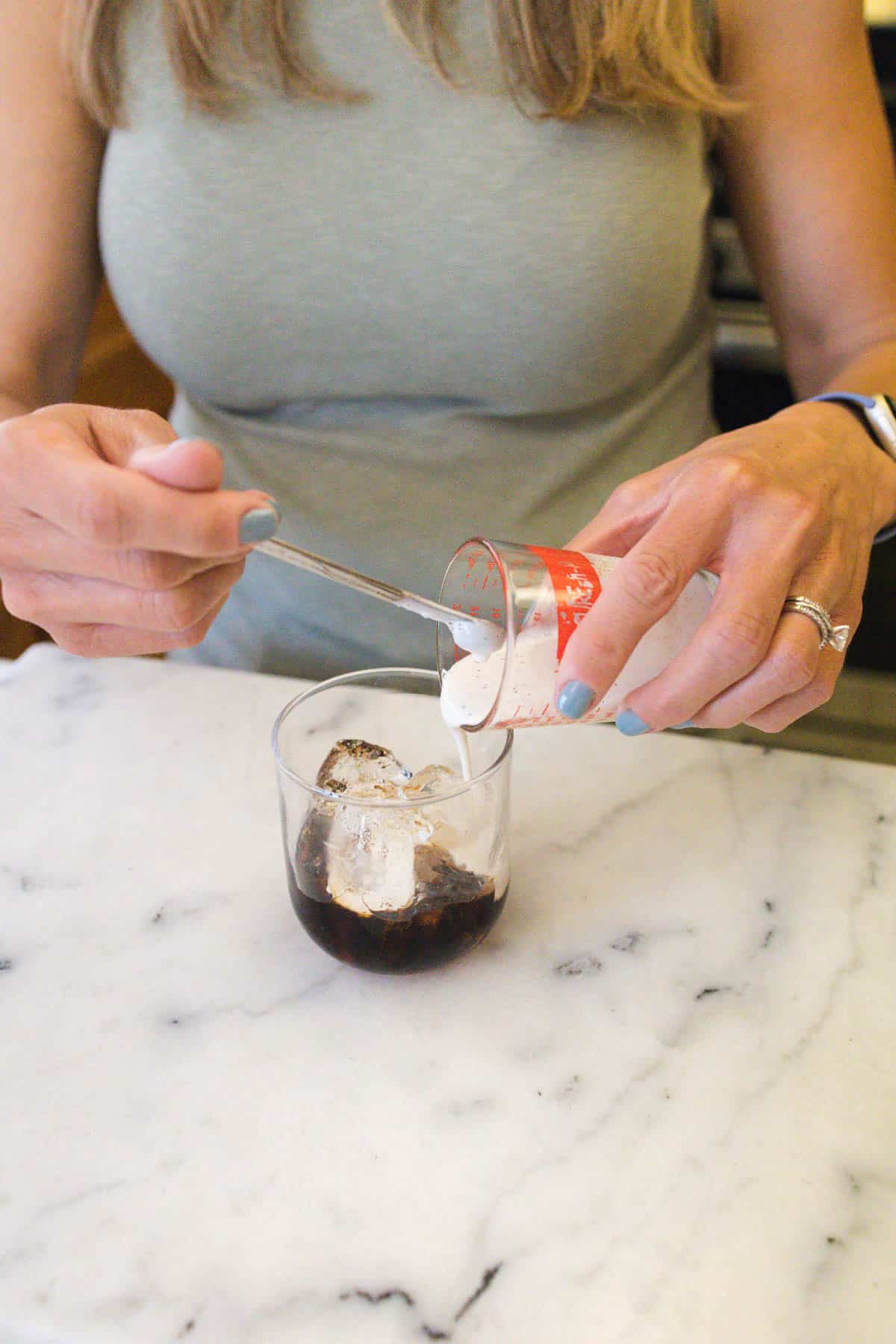 Woman pouring cream over a glass of Kahlua and ice.
