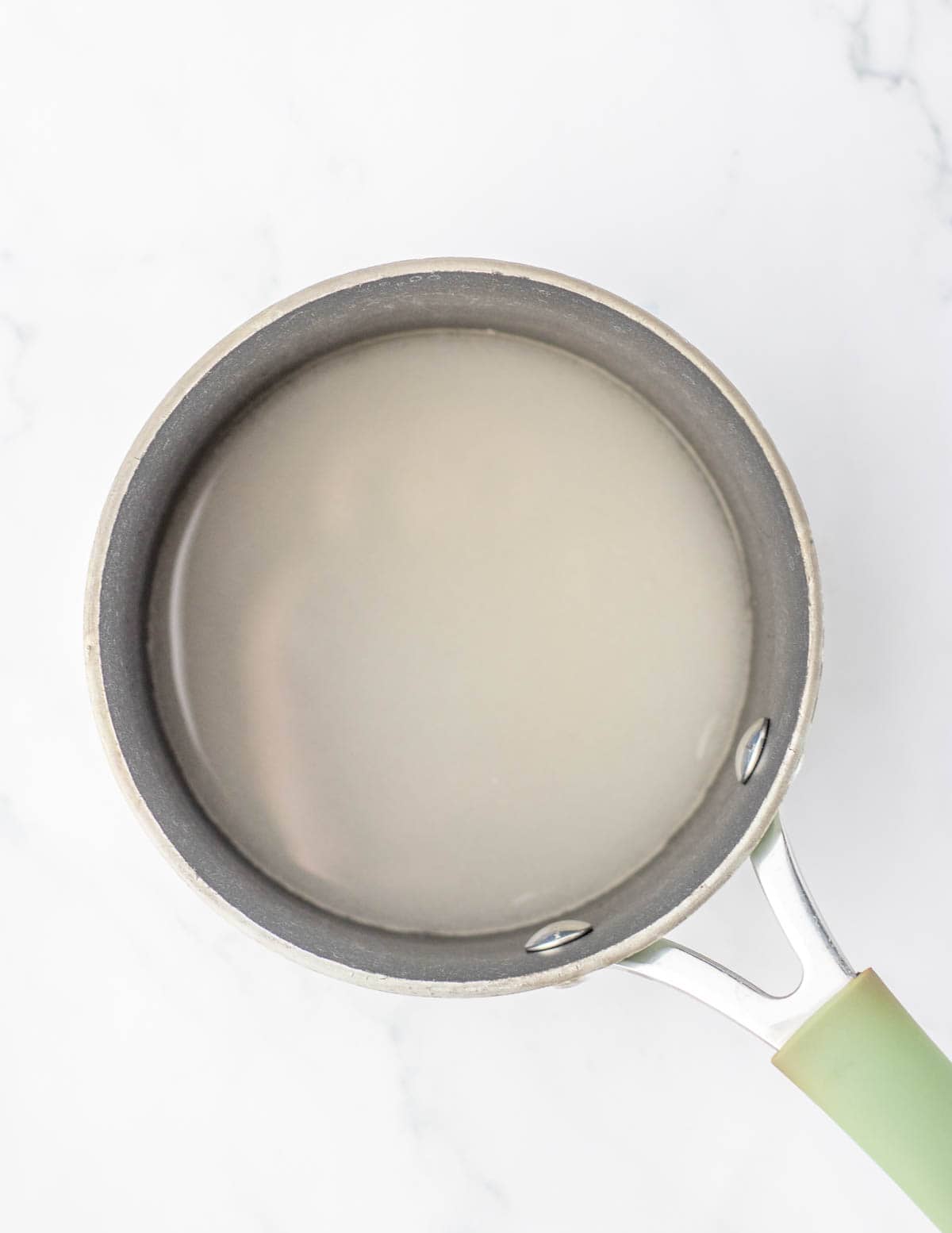 A sauce pan with sugar and water in it.