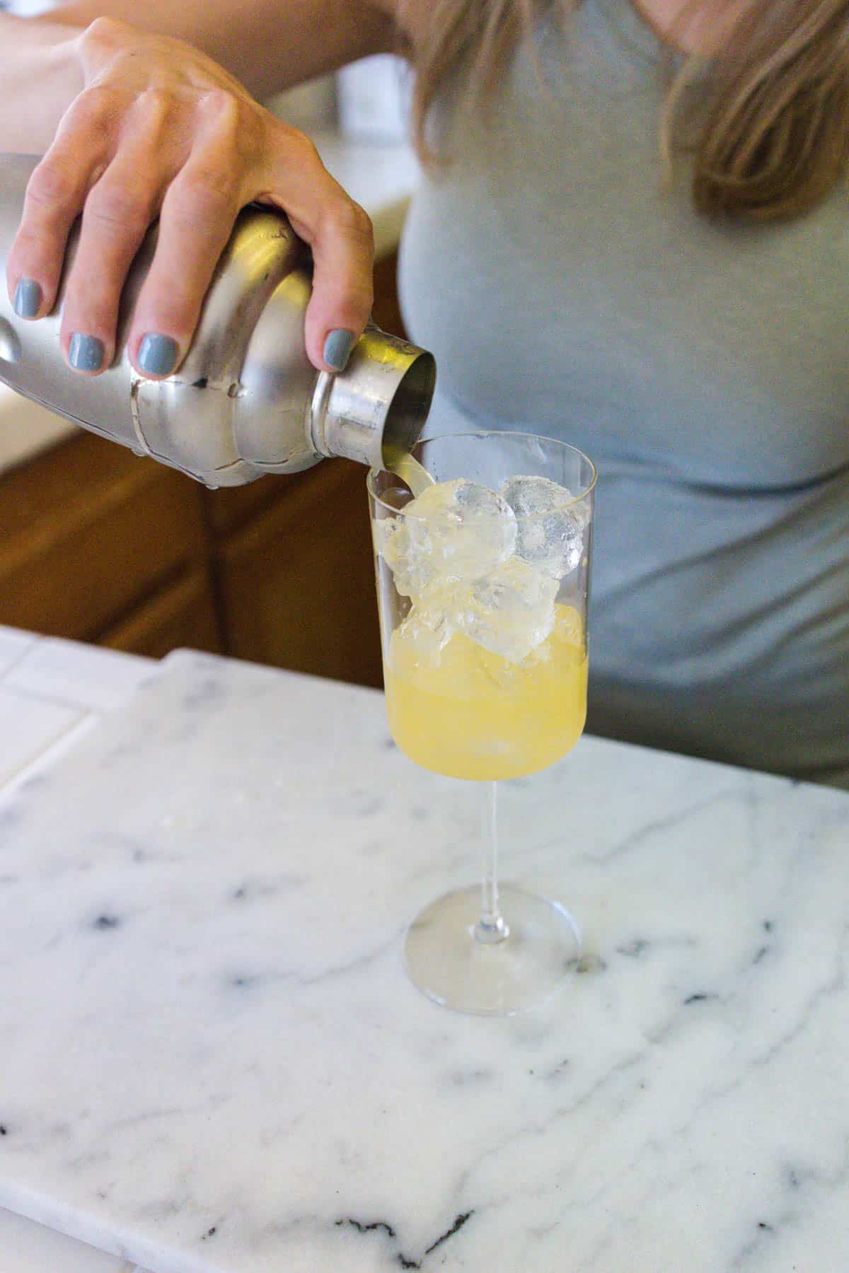 Tequila Spritzer being strained into a wine glass filled with ice.