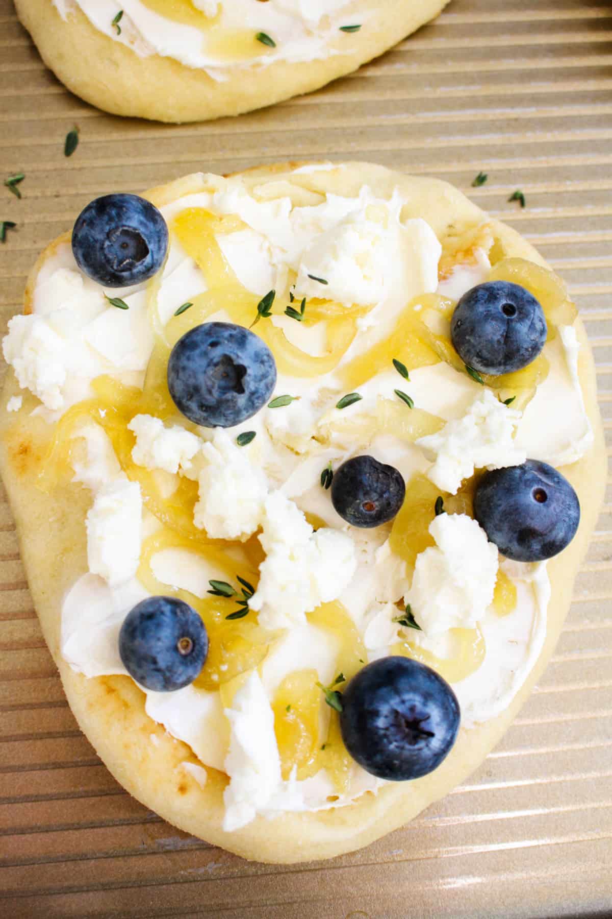 Flatbread appetizer with goat cheese, blueberries, honey, cream cheese, thyme, onions, and arugula.