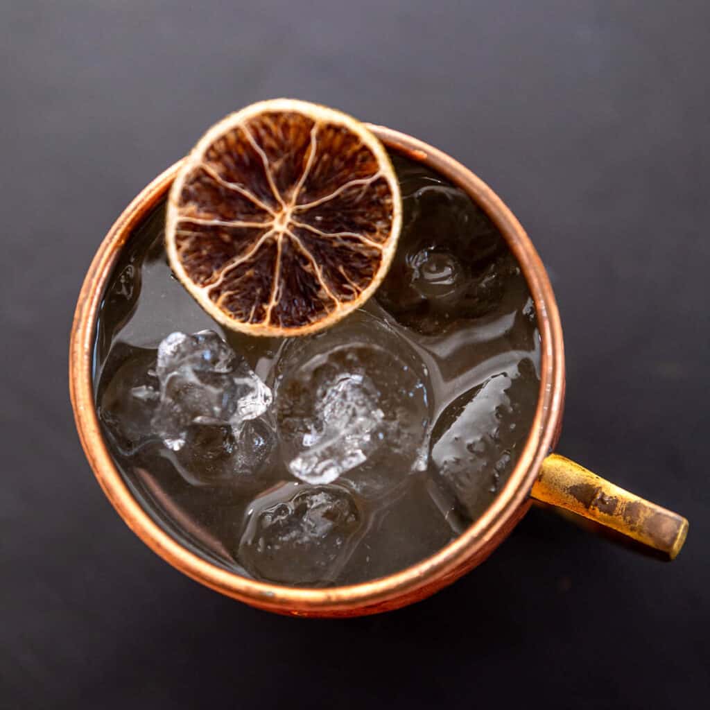 Close up of a Moscow Mule with a dried lime wheel pictured overhead on a dark background.