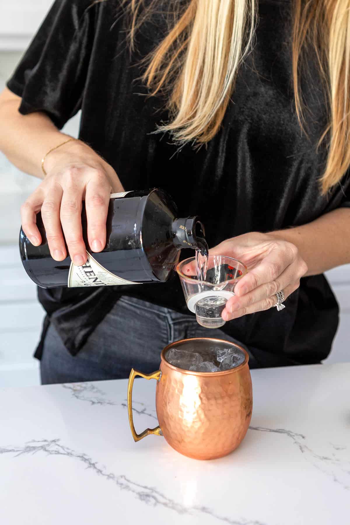 Woman measuring gin into a copper mule mug.