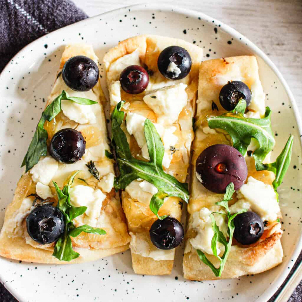 Sliced honey goat cheese flatbread on a white serving plate.