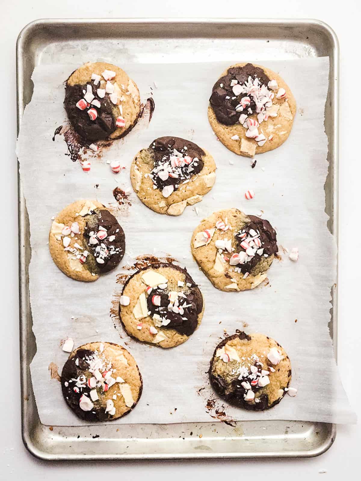 Baked chocolate marble cookies with crushed peppermint and white chocolate shavings on a parchment paper lined baking tray.