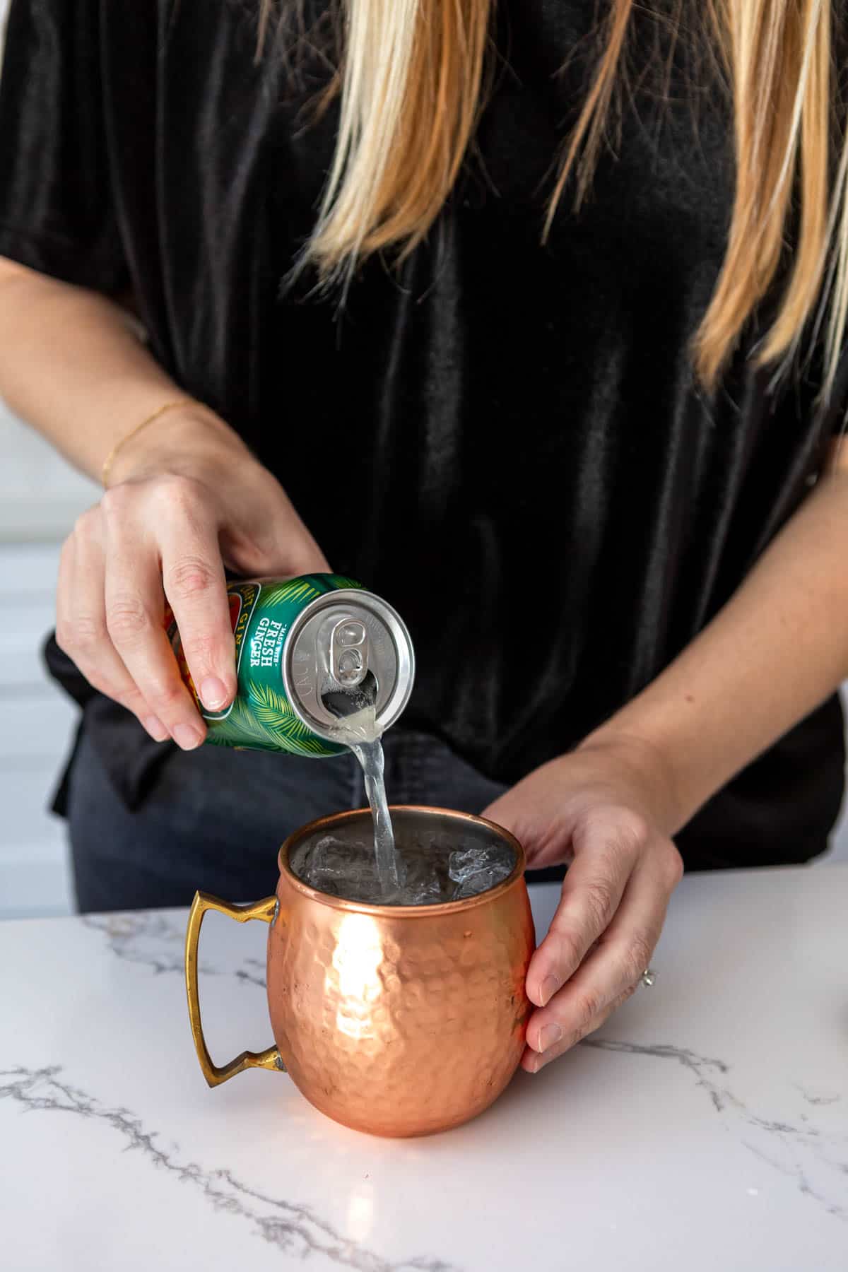Woman pouring a can of ginger beer into a copper mule mug.