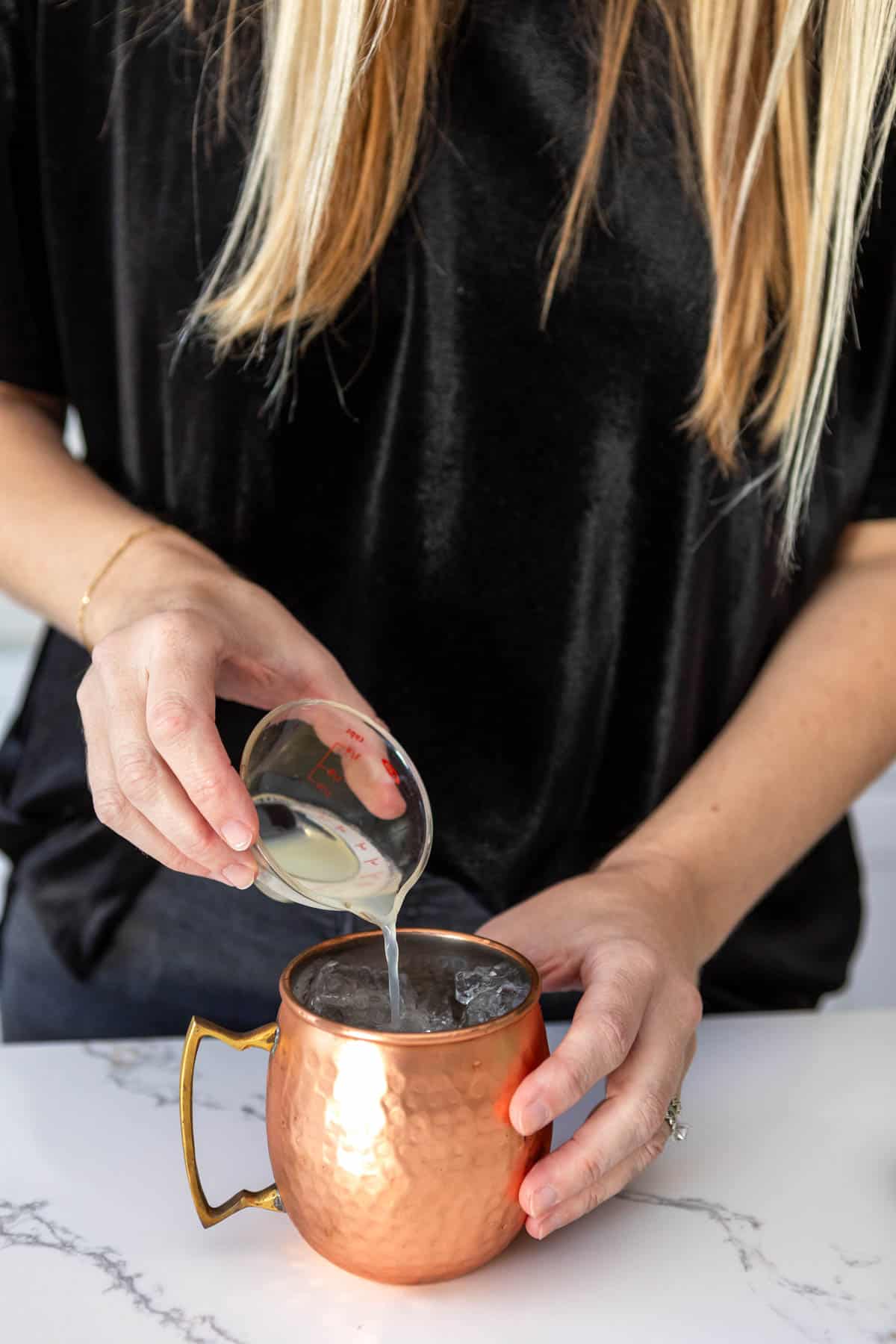 Woman measuring lime juice into a copper mule mug.
