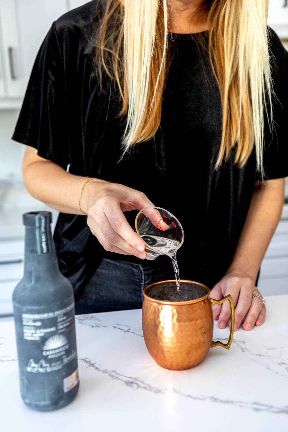 Woman pouring a measure of mezcal into a copper mule mug.