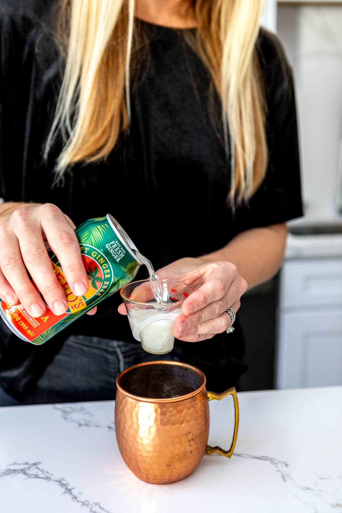 Woman measuring ginger beer into a copper mule mug.