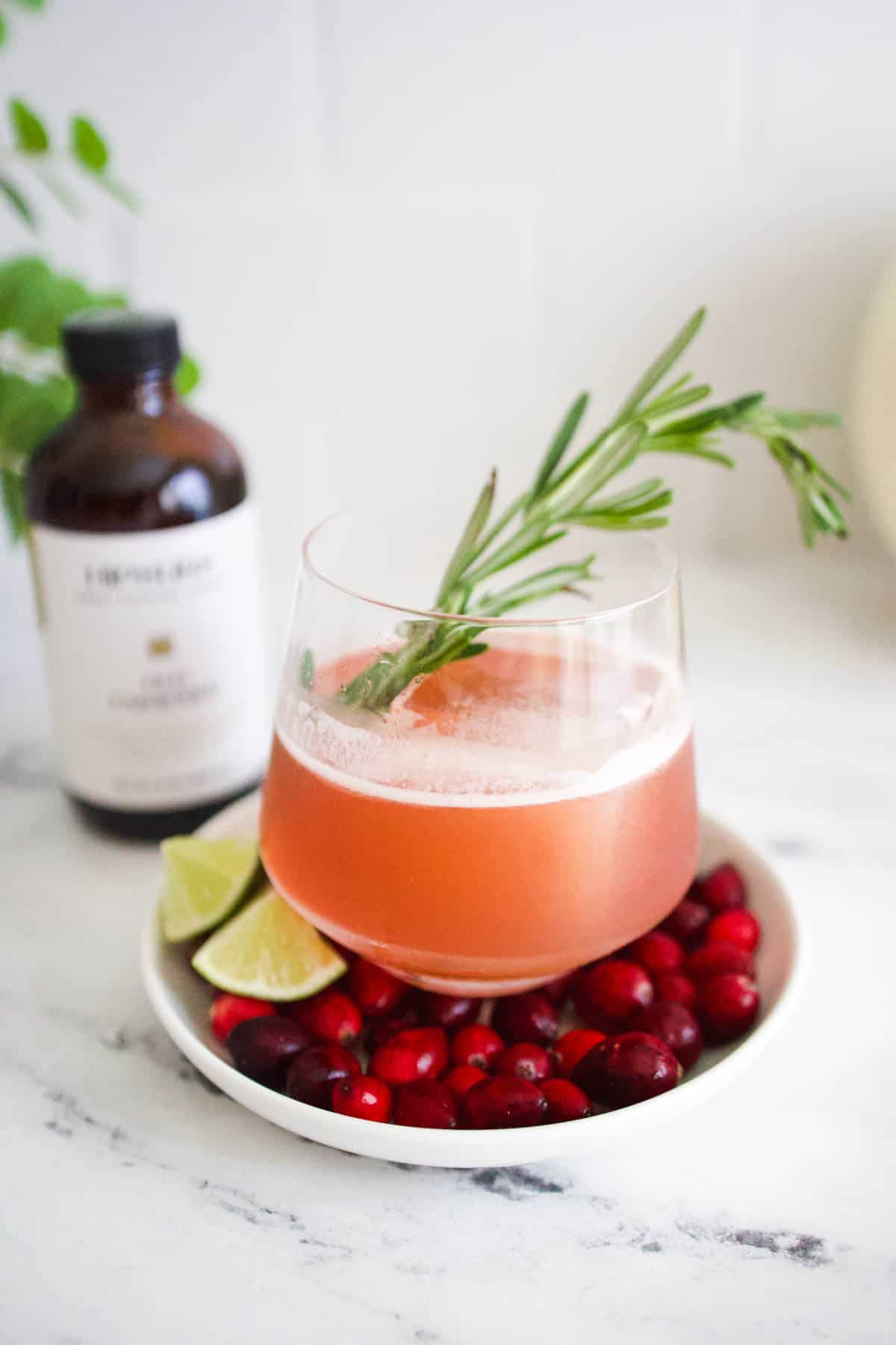 A cranberry bourbon old fashioned in a short cocktail glass on a small tray of fresh cranberries.