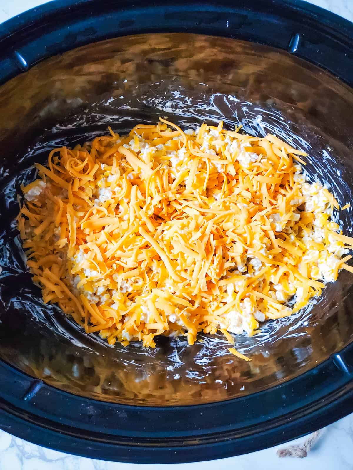 Creamed corn topped with cheese in a crockpot.