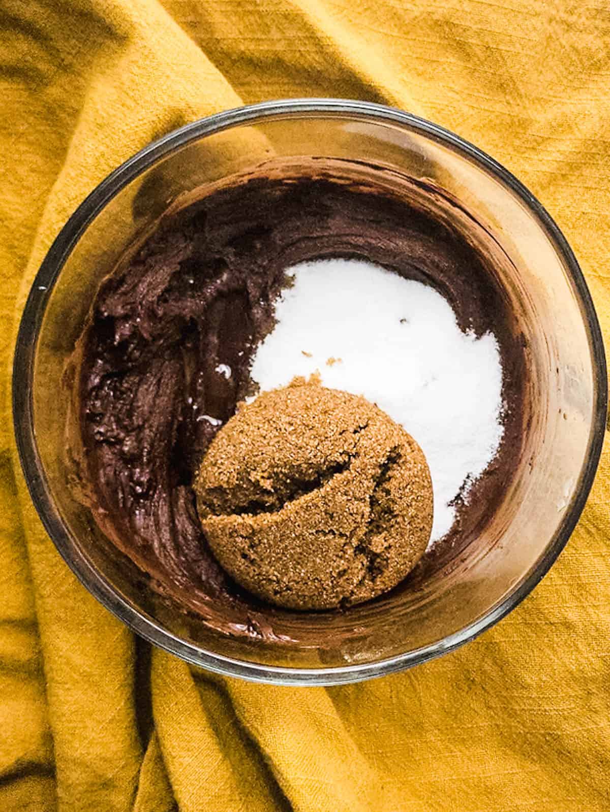 Brown sugar and white sugar into the chocolate batter in a glass mixing bowl.