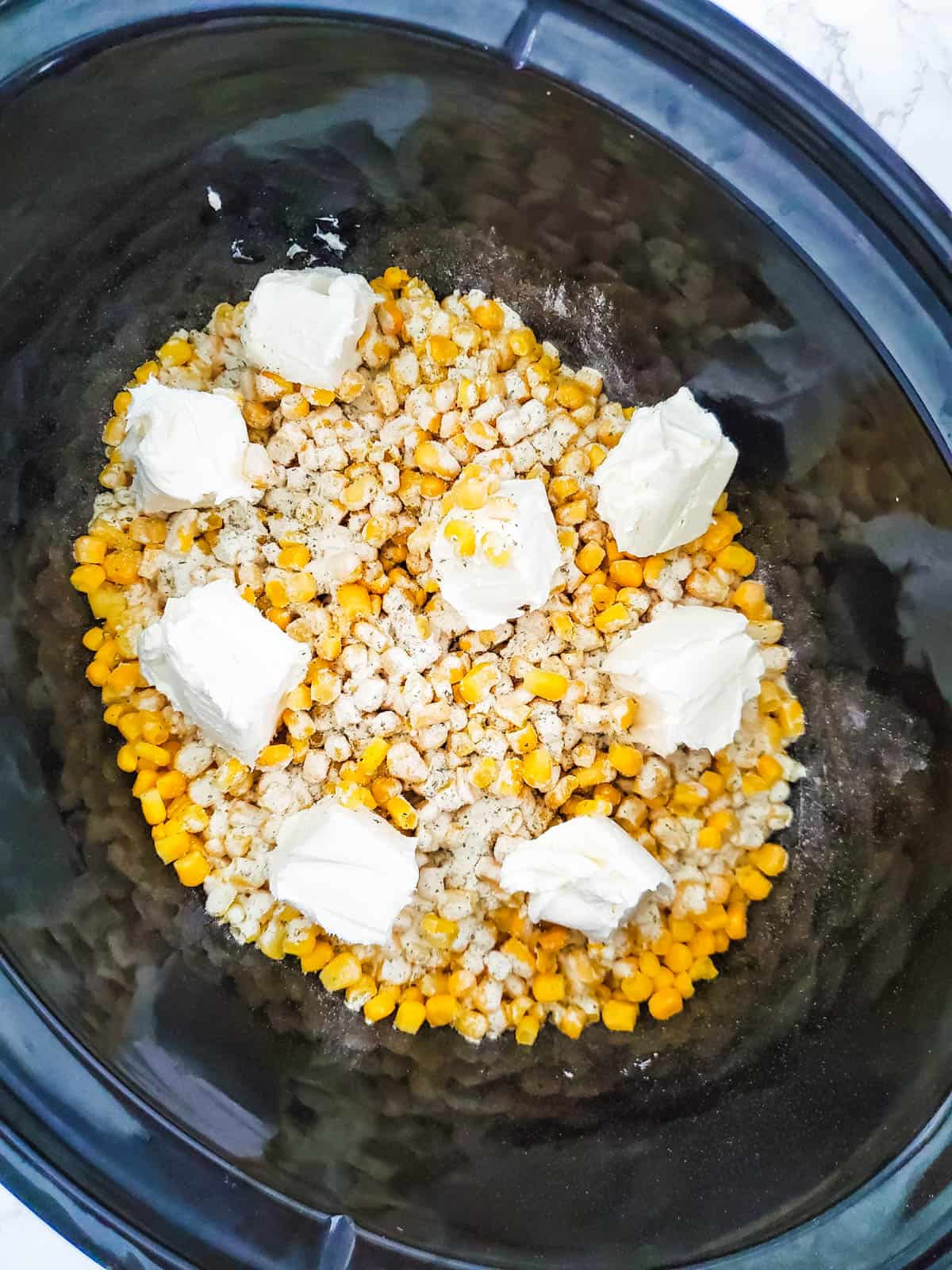 Corn in a crockpot topped with cubed cream cheese.