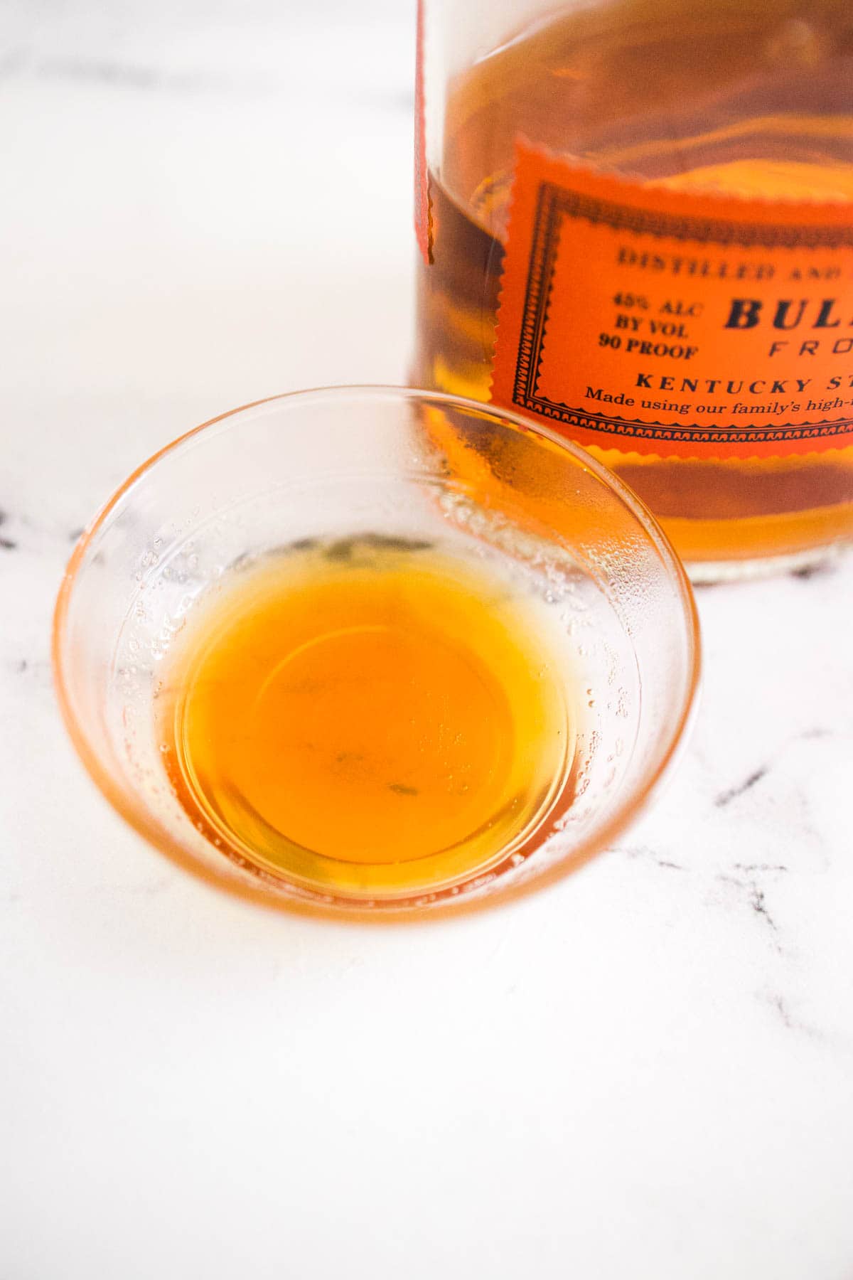 A close up of a small bowl of honey on a table next to a bottle of bourbon.