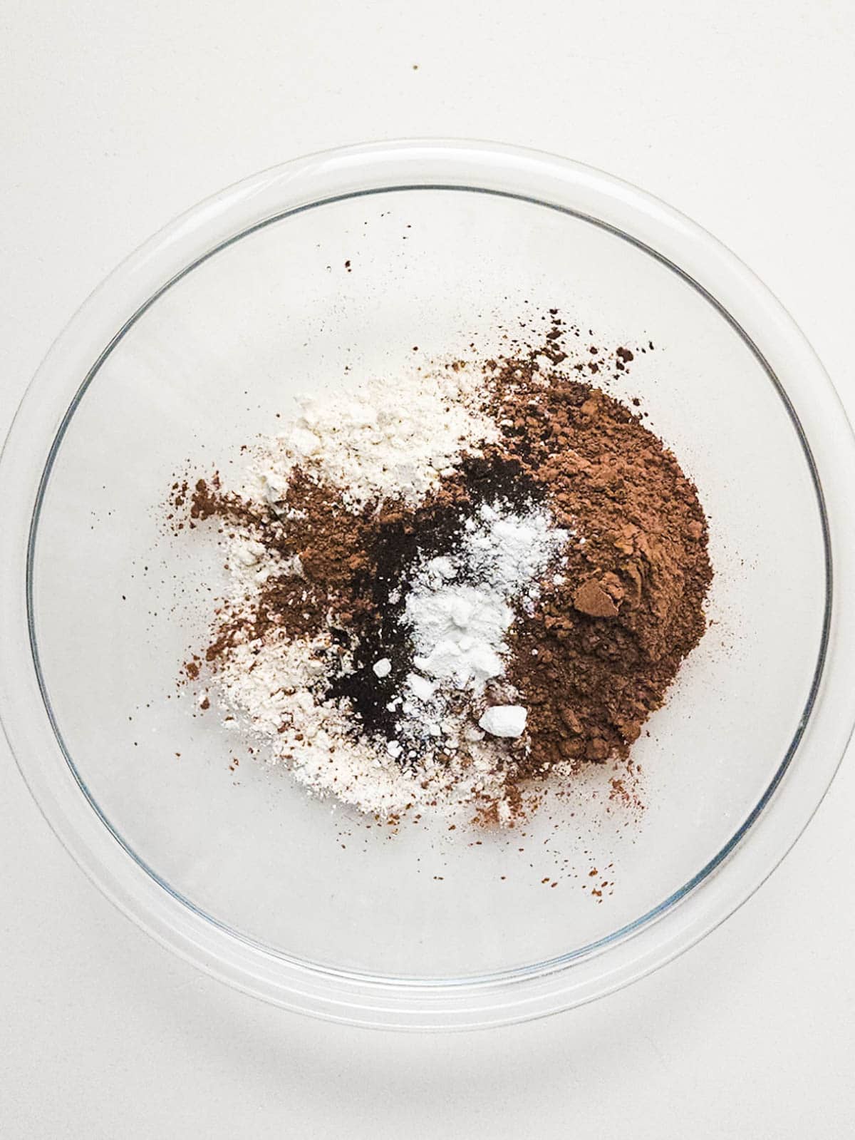 Dry ingredients for chocolate cookie batter on a glass bowl on the table.