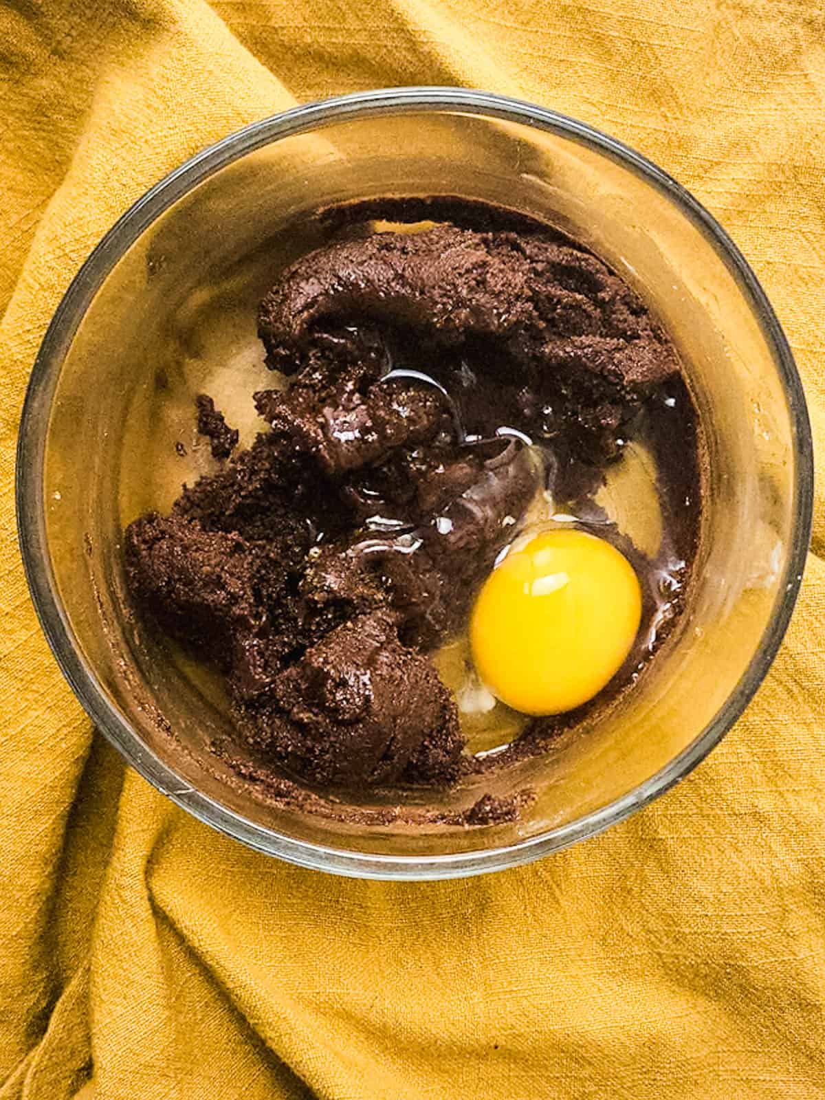 A cookie batter in a glass bowl with a raw egg.