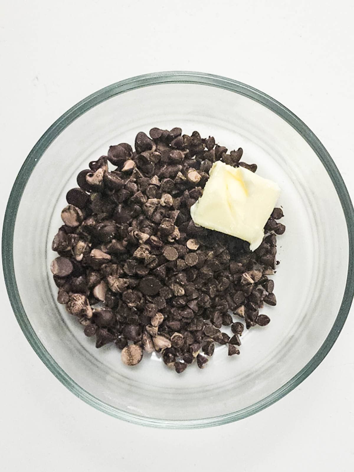 Dark chocolate chips and butter on a glass mixing bowl.