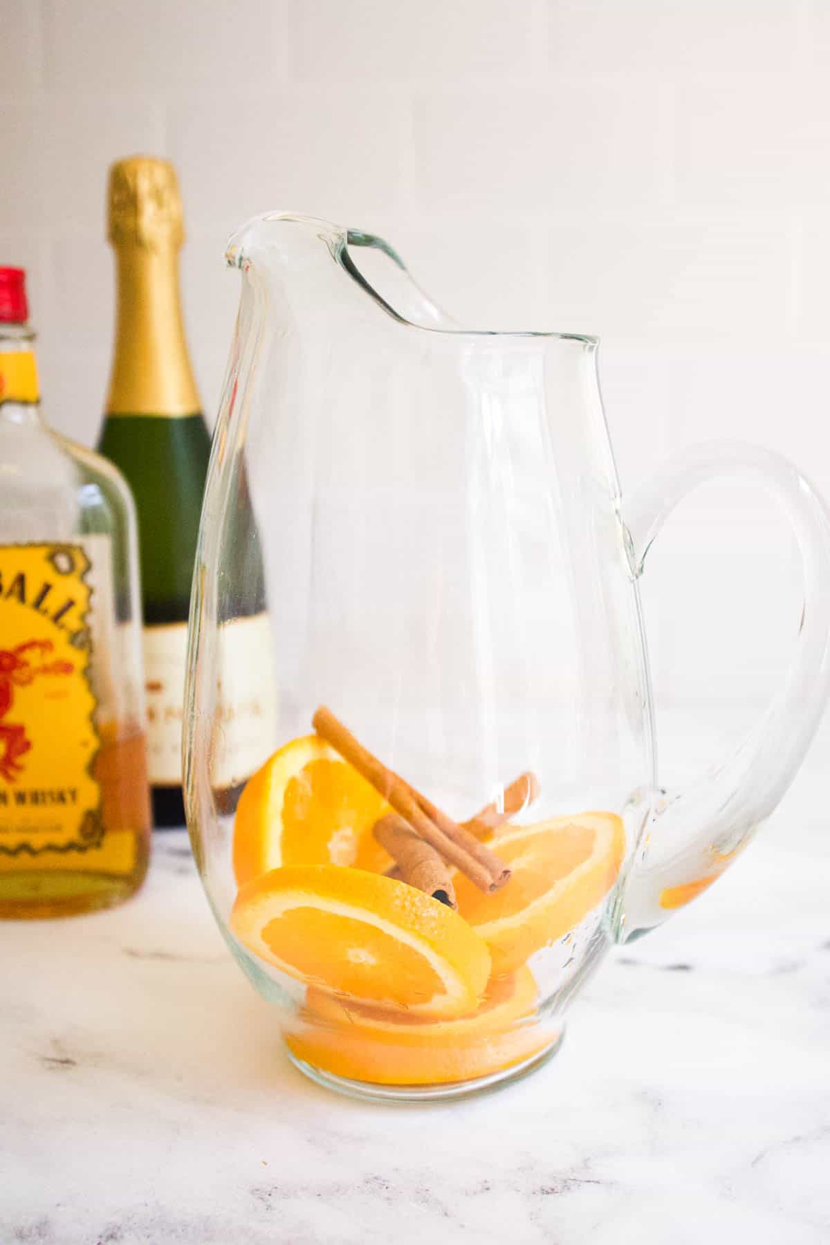 Sliced oranges and cinnamon sticks in the bottom of a pitcher. 