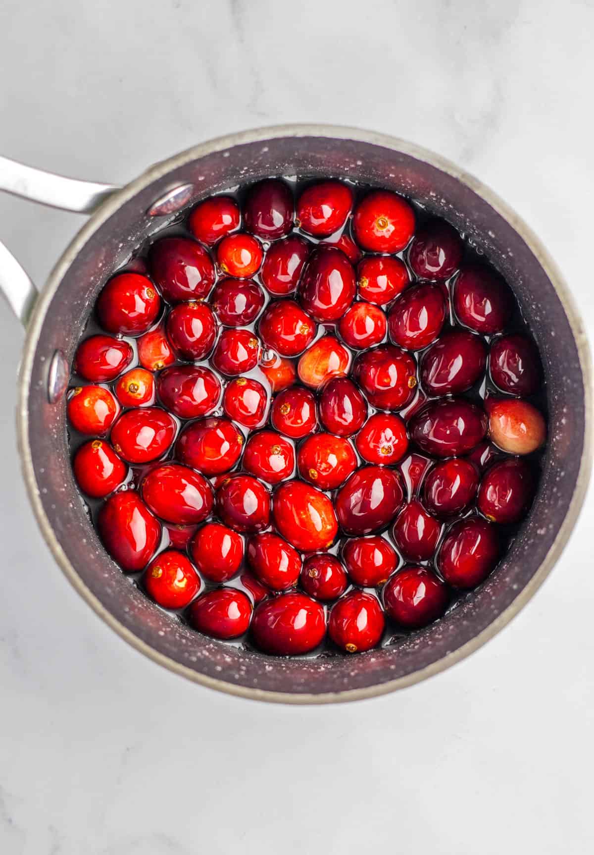 A sauce pan with sugar syrup and fresh cranberries.