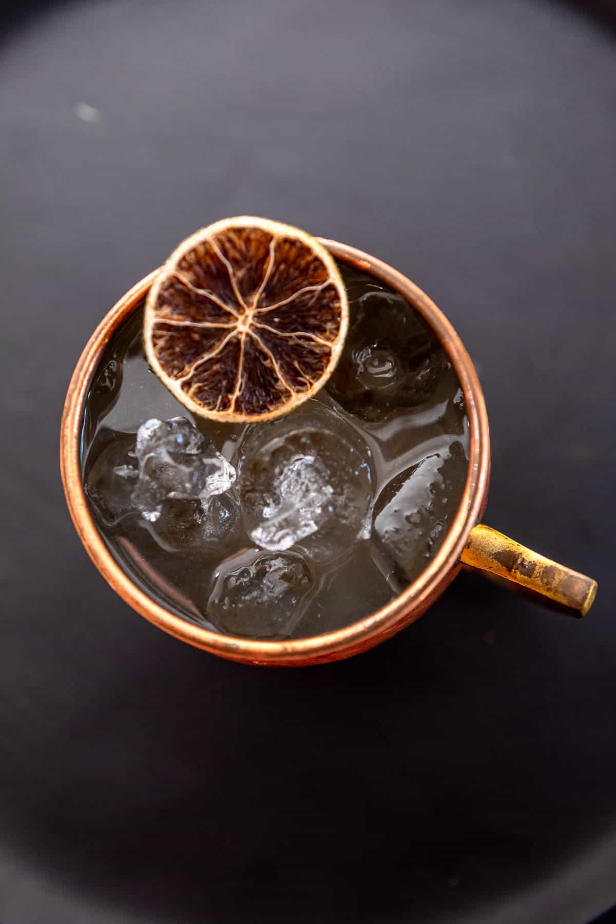 Overhead photo of a gin mule garnished with a dried lime wheel on a dark background.