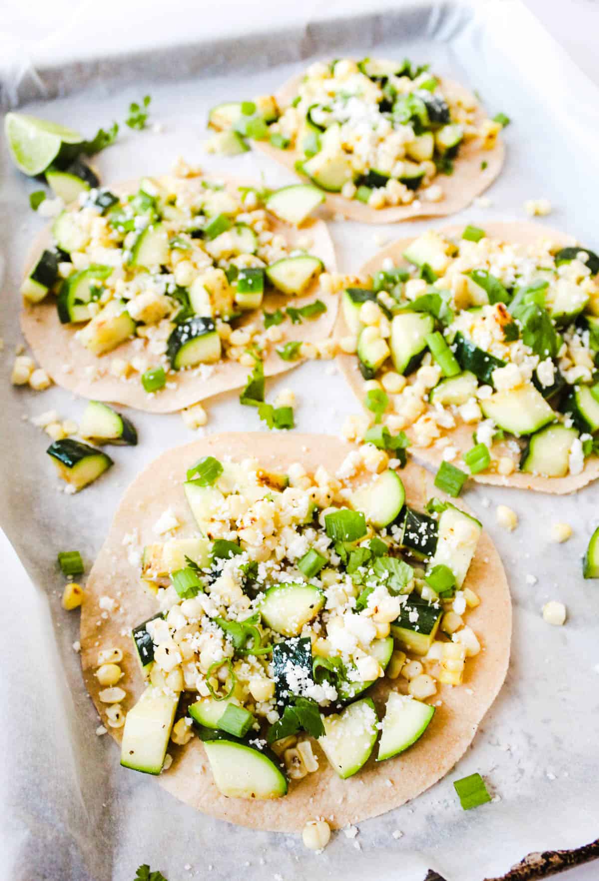 Close up picture of zucchini and corn tostadas topped with cotija cheese and green onions.