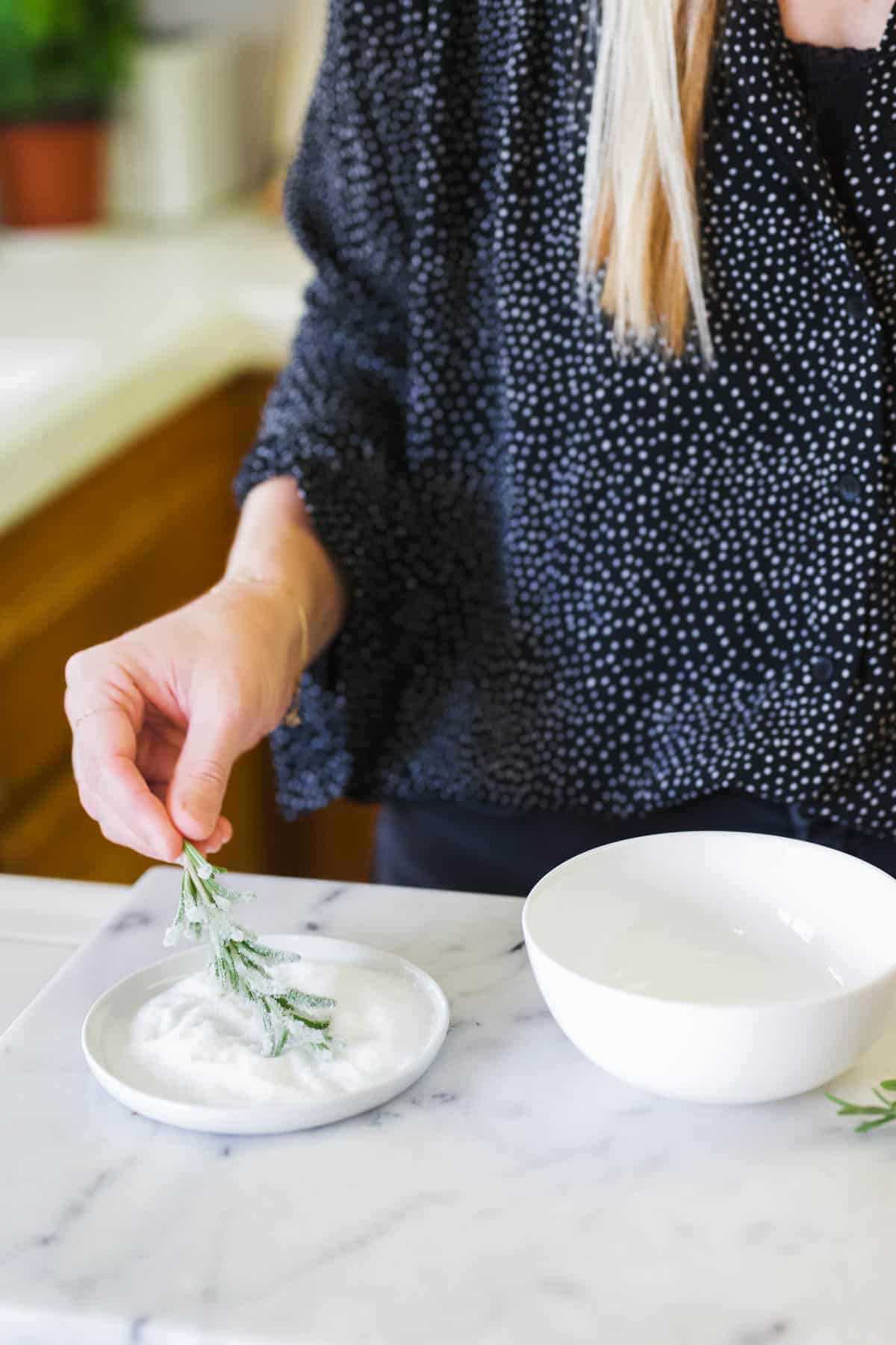 Dipping rosemary sprig into white granulated sugar.