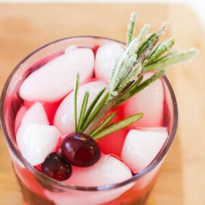 Sugared rosemary garnish on a red drink in a glass.