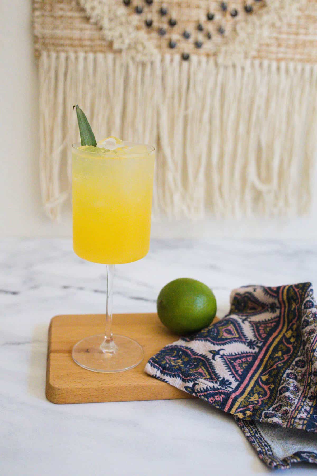 Tequila spritzer in a wine glass on a wooden board with a whole lime.