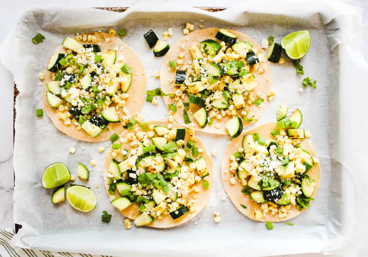 Delicious zucchini and corn tostadas on a parchment lined baking tray.