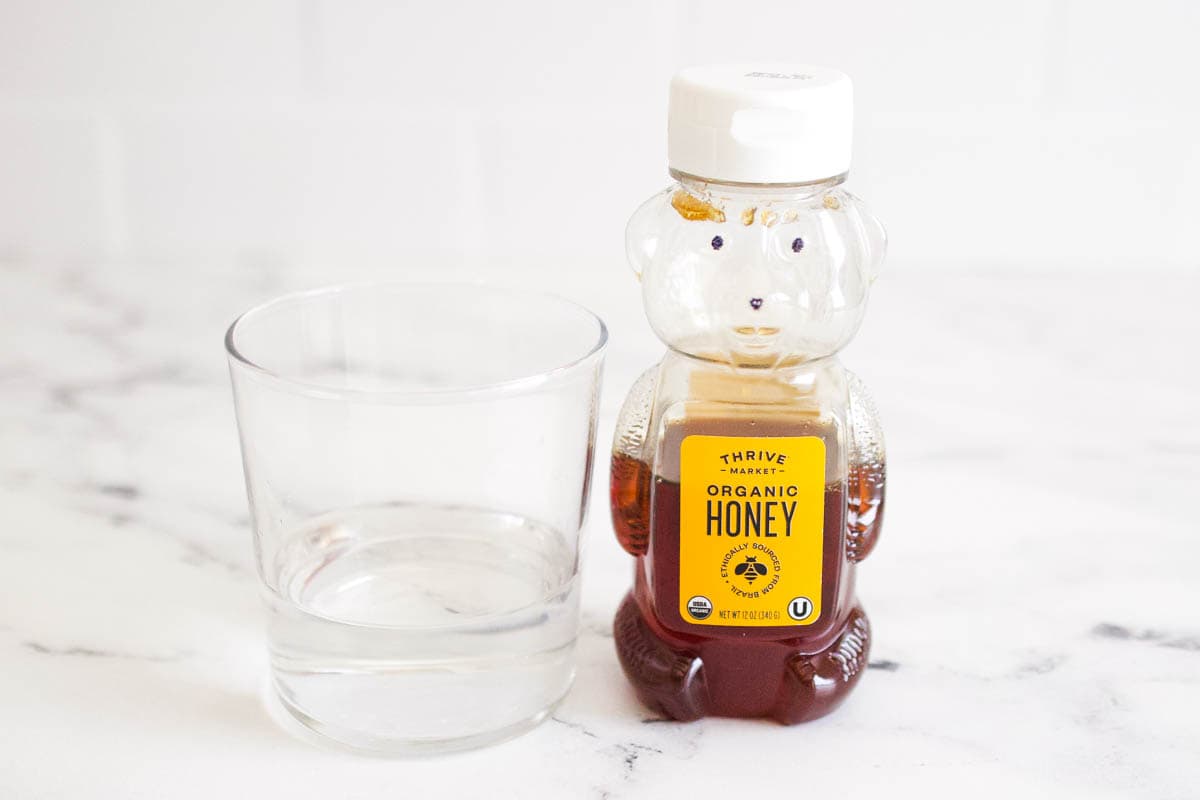 A glass of water next to a bottle shaped like a bear filled with honey.