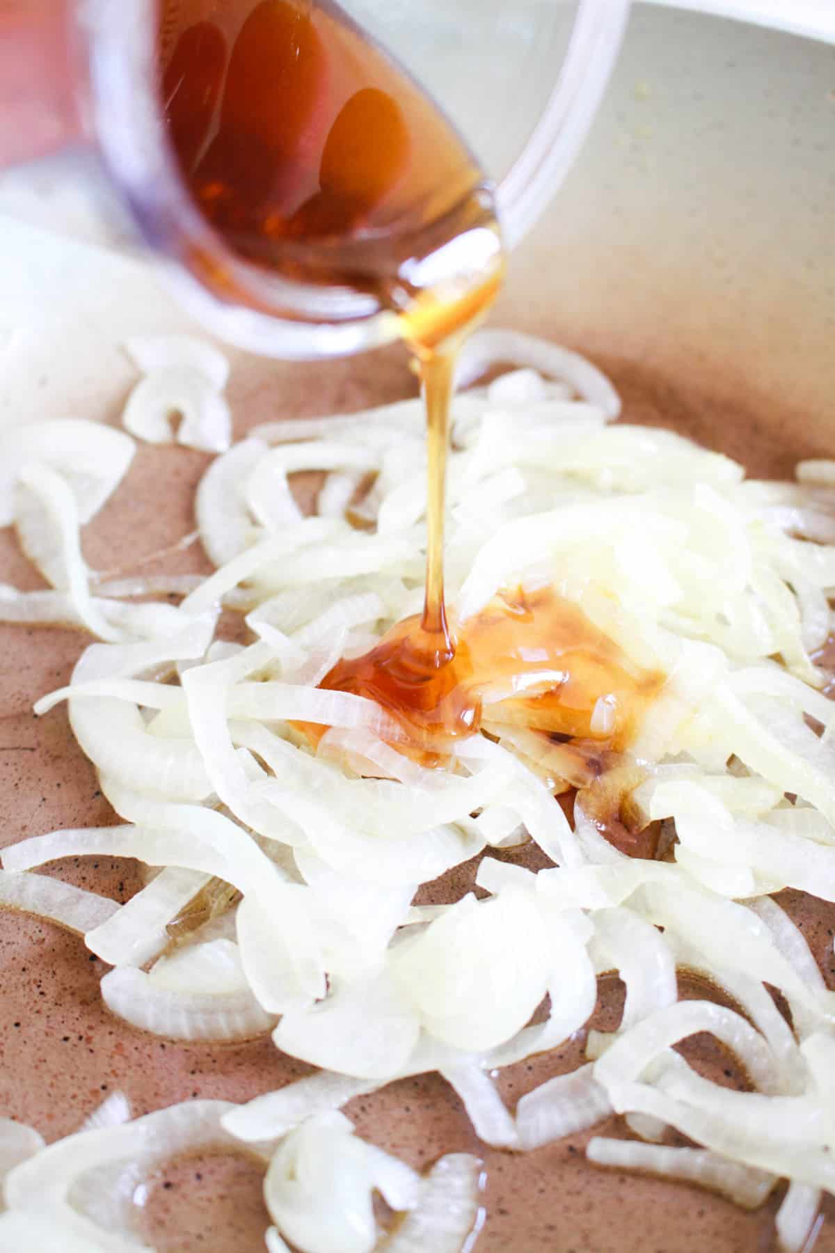 Pouring honey on sliced white onions on a sautee pan.