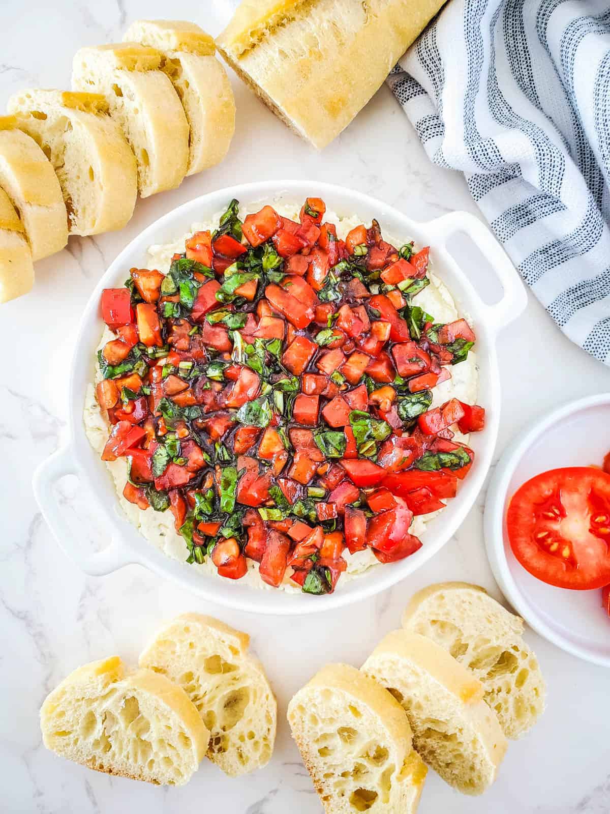 A bowl on a table holding a boursin bruschetta dip for a party with sliced baguette around it.