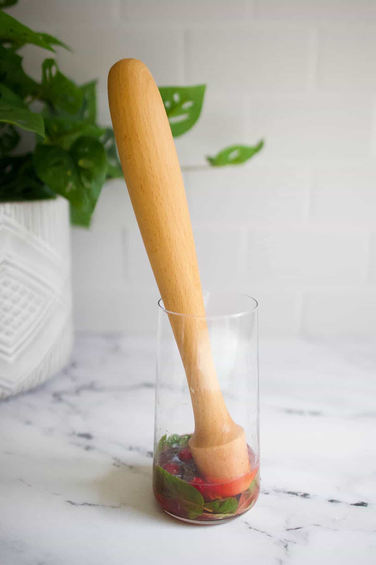 muddle ingredients Cranberries, mint and lime being muddled in the bottom of a glass.