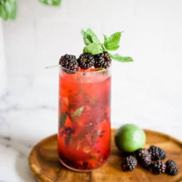 Blackberry mojito garnished with fresh blackberries and mint on a wooden board.