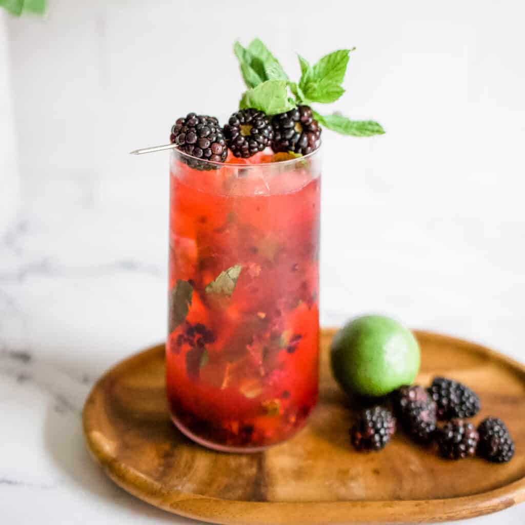 Blackberry mojito on a wooden serving board with fresh blackberries and a whole lime.