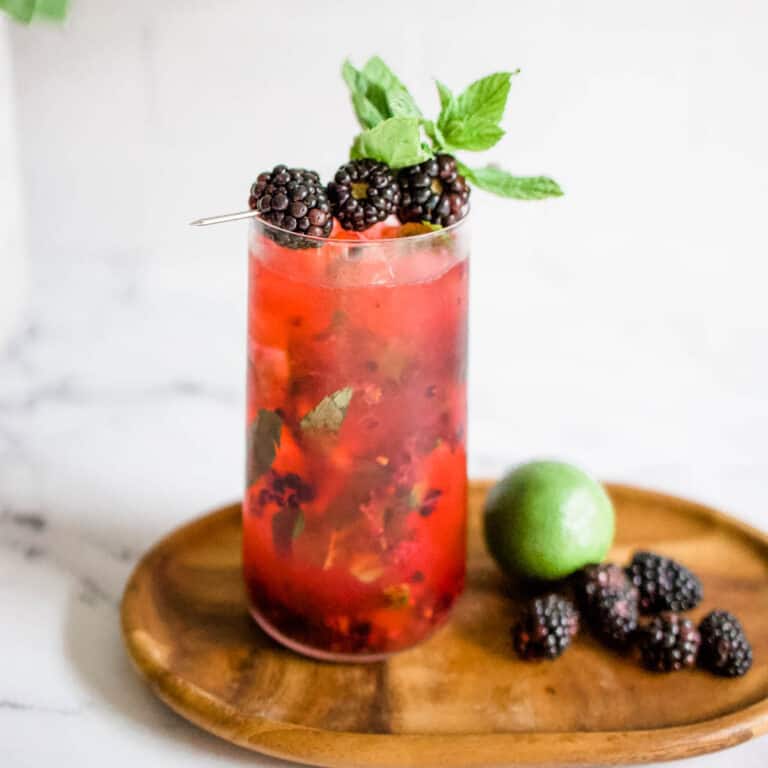 Blackberry mojito on a wooden serving board with fresh blackberries and a whole lime.