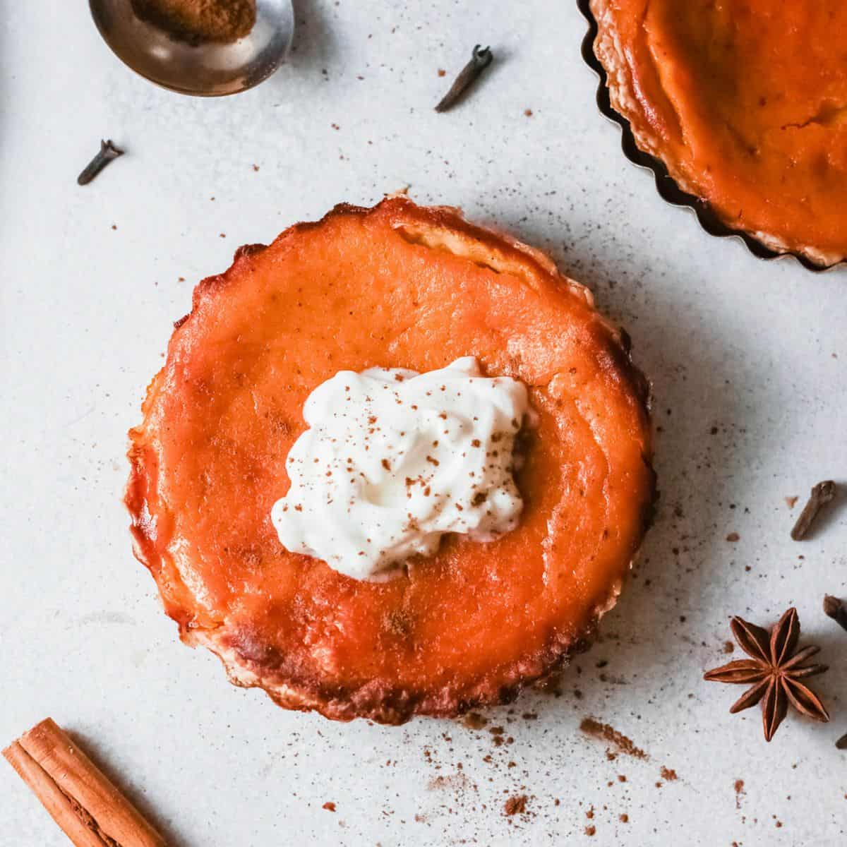 Fireball pumpkin pie topped with whipped cream on a table next to cinnamon sticks.