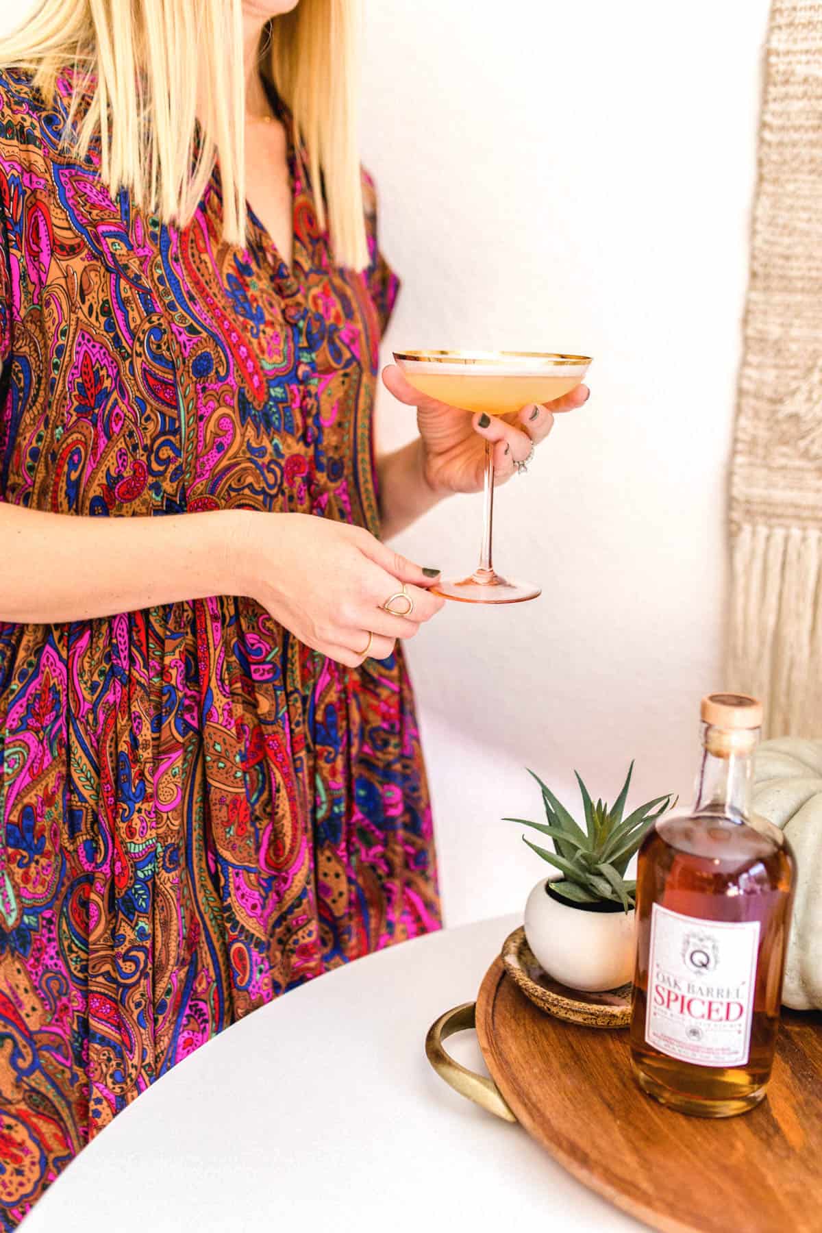 Woman holding a martini glass next to a table iwth a bottle of rum on it.