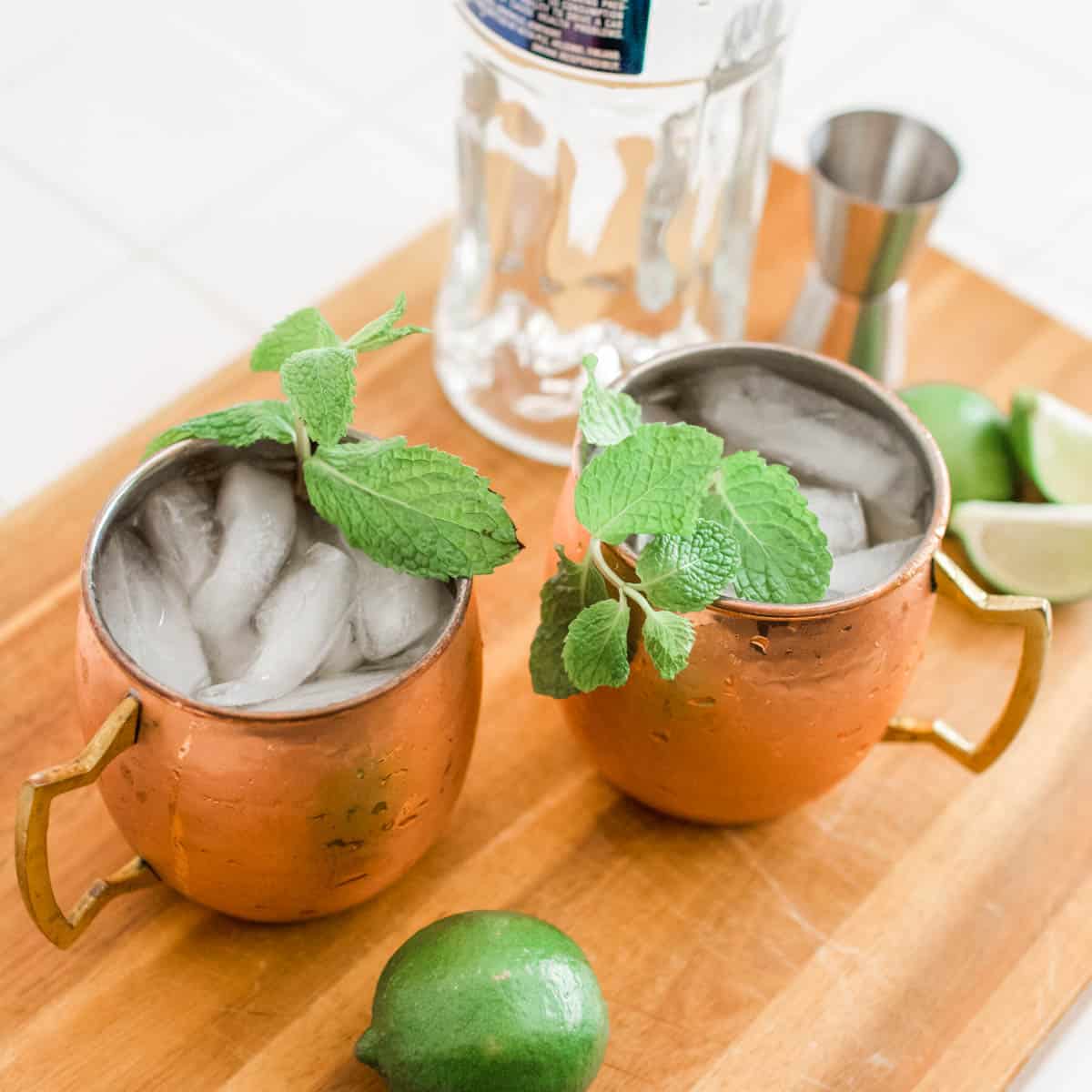 Cocktails in copper mugs on a counter next to a bottle of vodka.