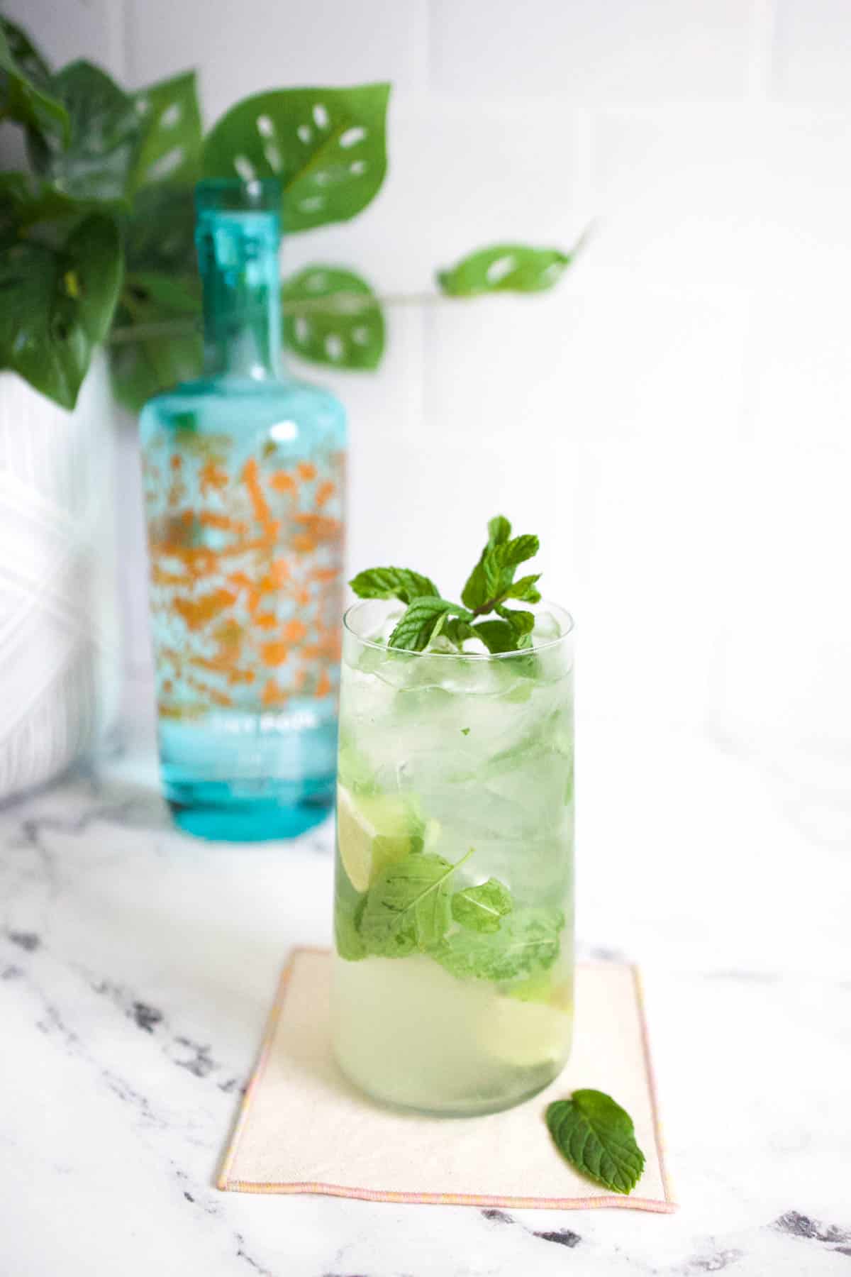 Mojito with Gin recipe Gin mojito on a white marble countertop with a blue bottle of gin in the background.
