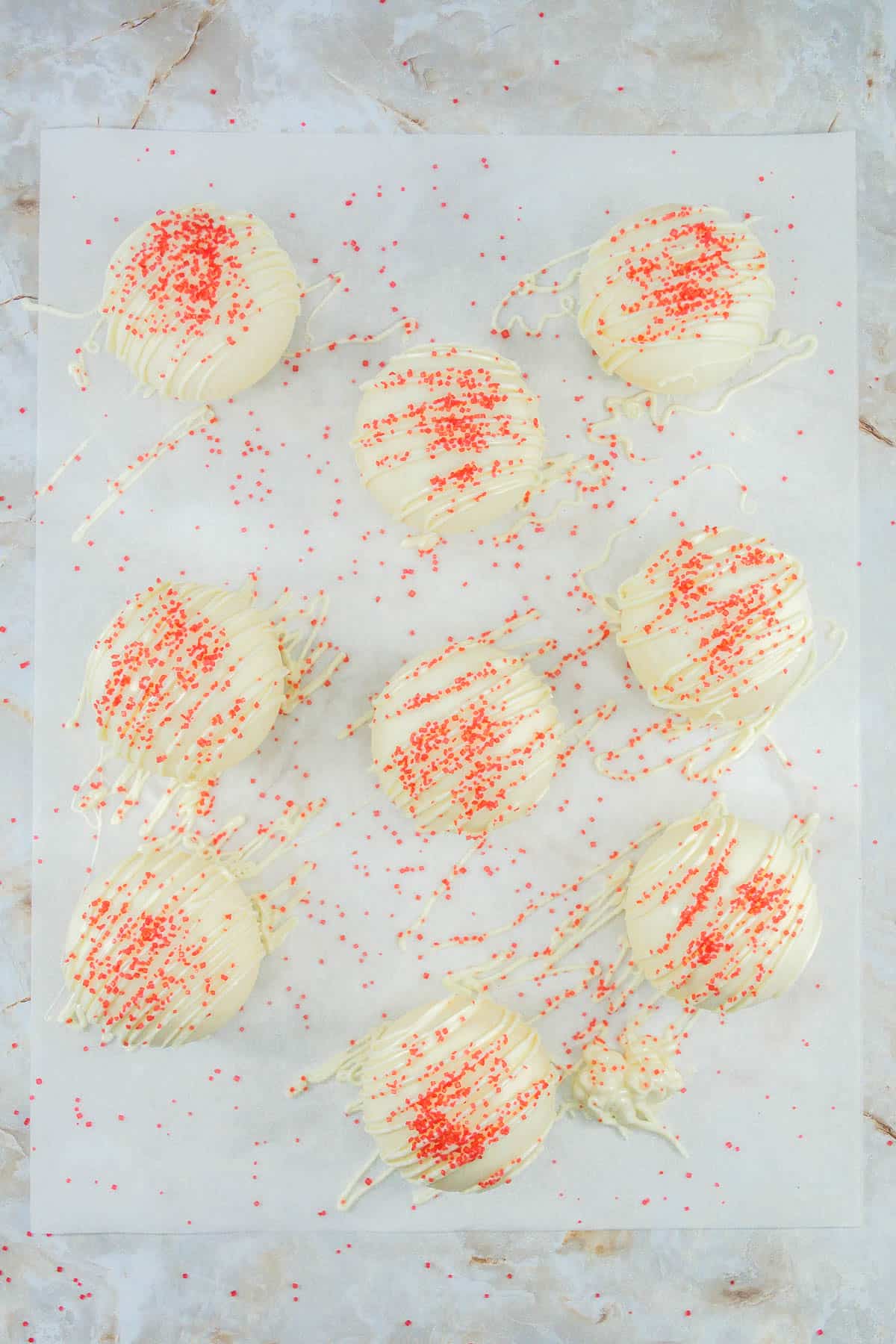Fireball Hot Chocolate Bombs on a piece of baking parchment decorated with melted chocolate drizzles and red sanding sugar.