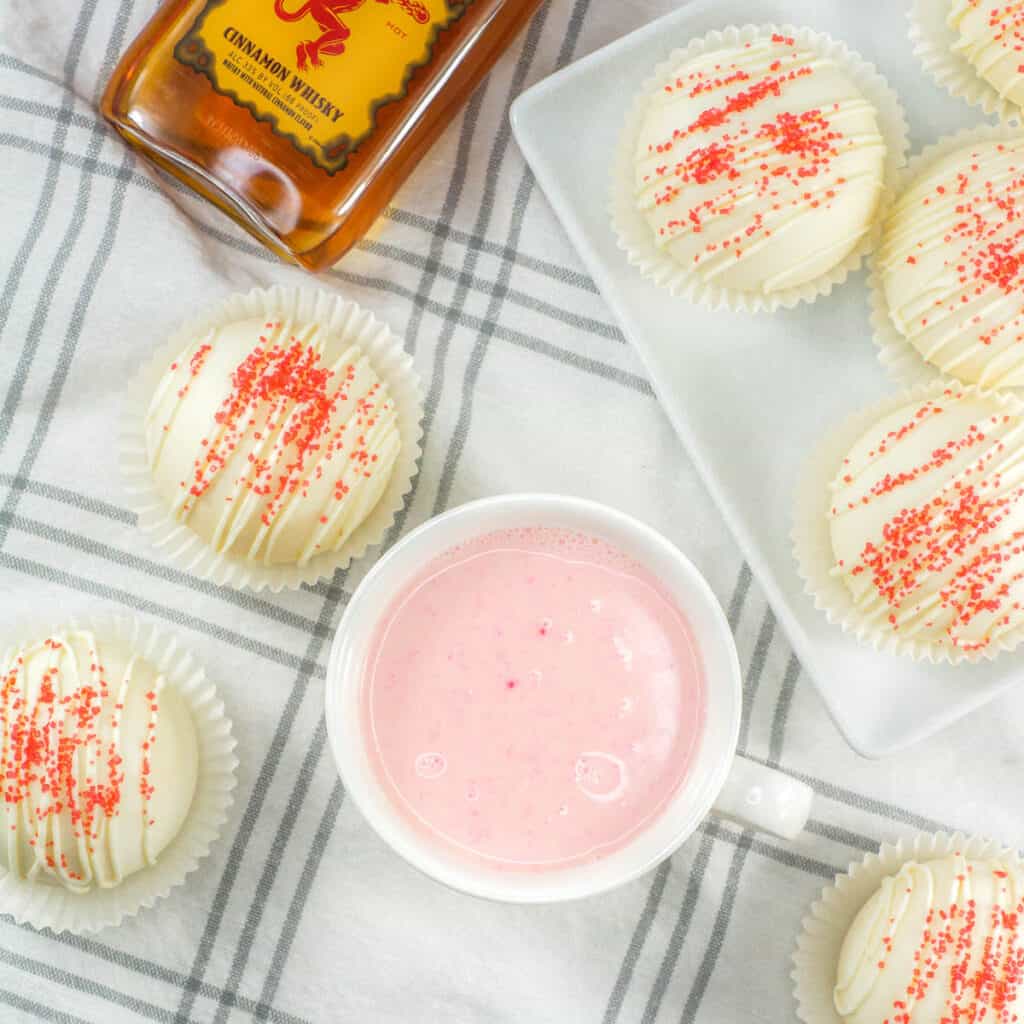 Close up of Fireball white chocolate cocoa bombs and a mug of pink hot cocoa.