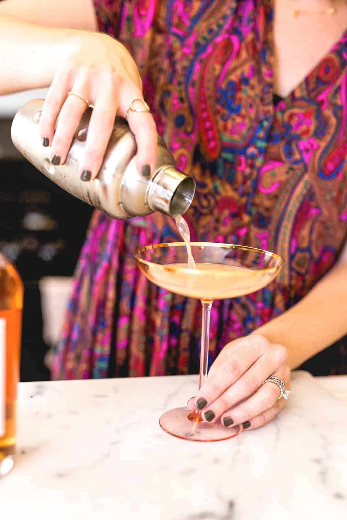 Woman pouring a cocktail into a martini glass.