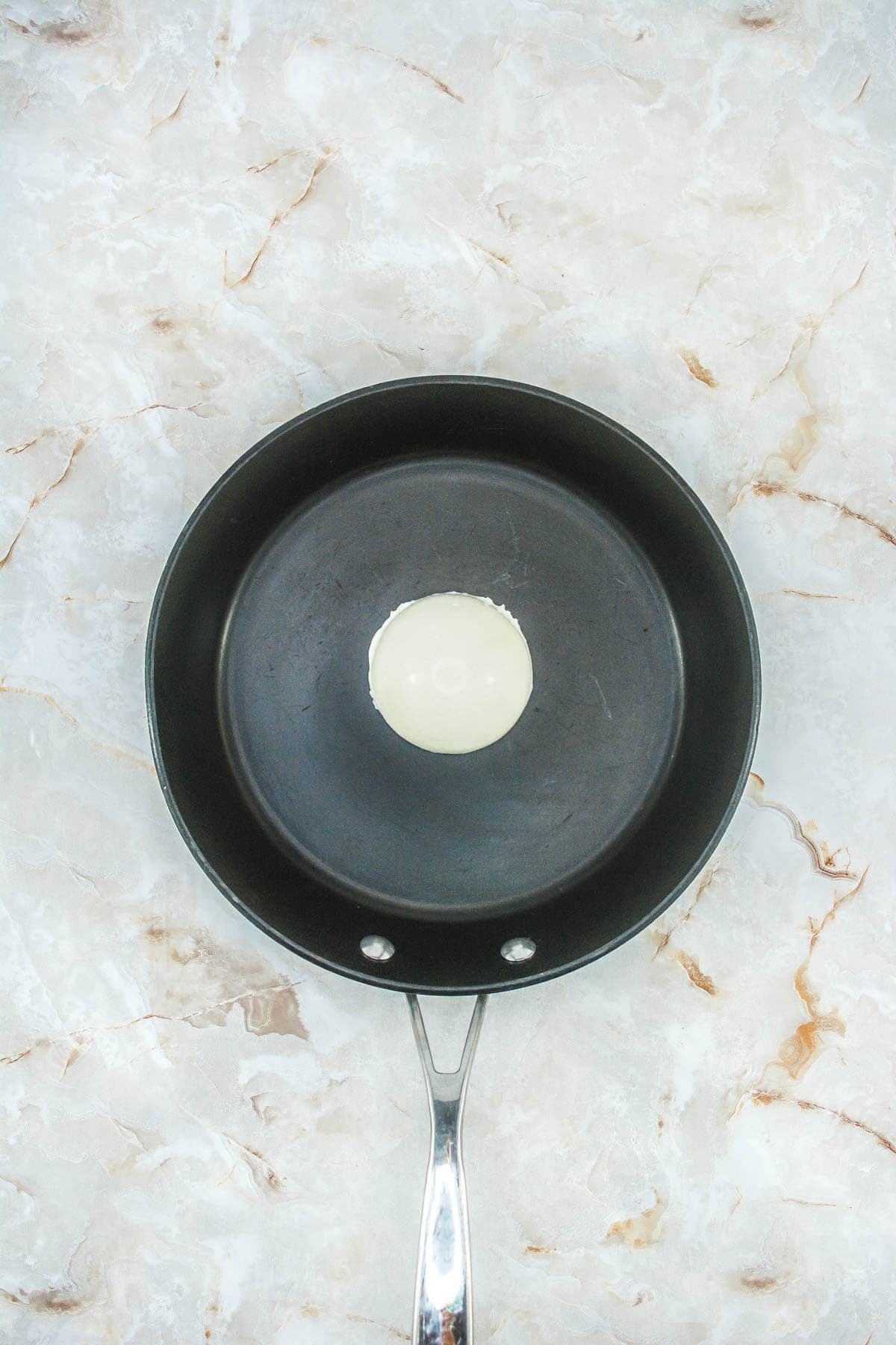 A half sphere of white chocolate upside down in a frying pan.