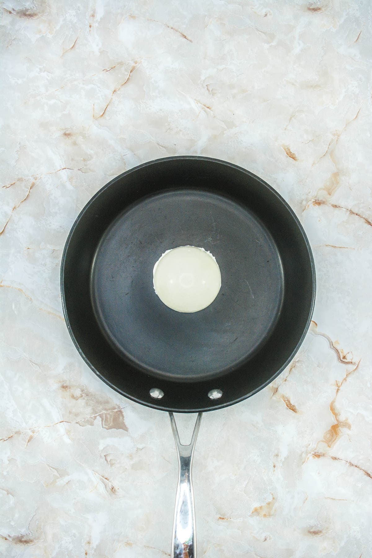 A half sphere of white chocolate upside down in a frying pan.