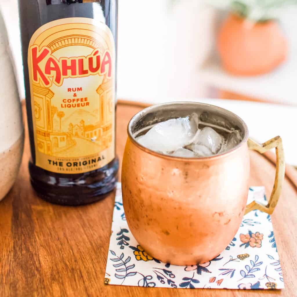 Close up of a mule mug with a bottle of Kahlua in the background.