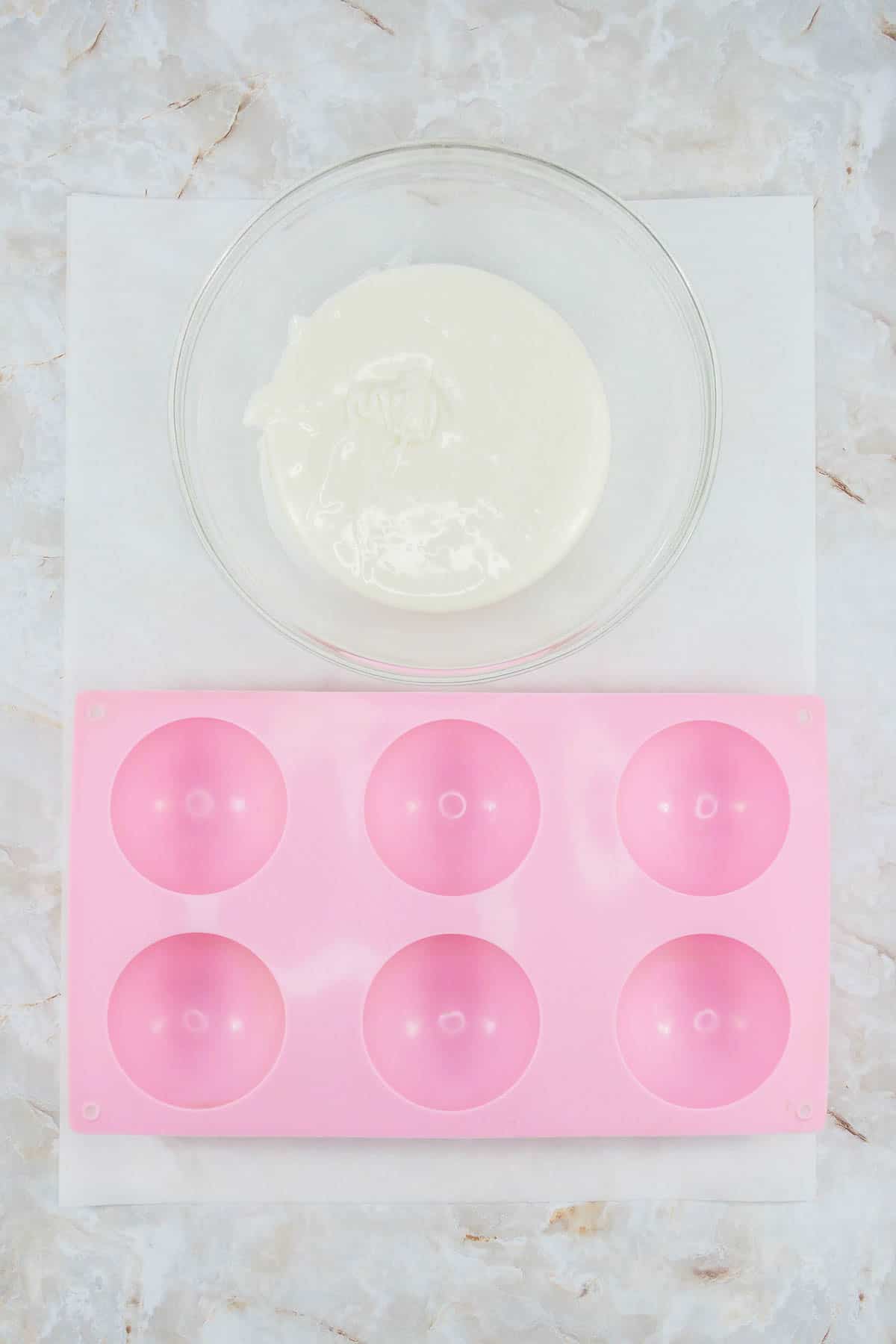 A bowl of melted white chocolate next to a pink silicone mould.