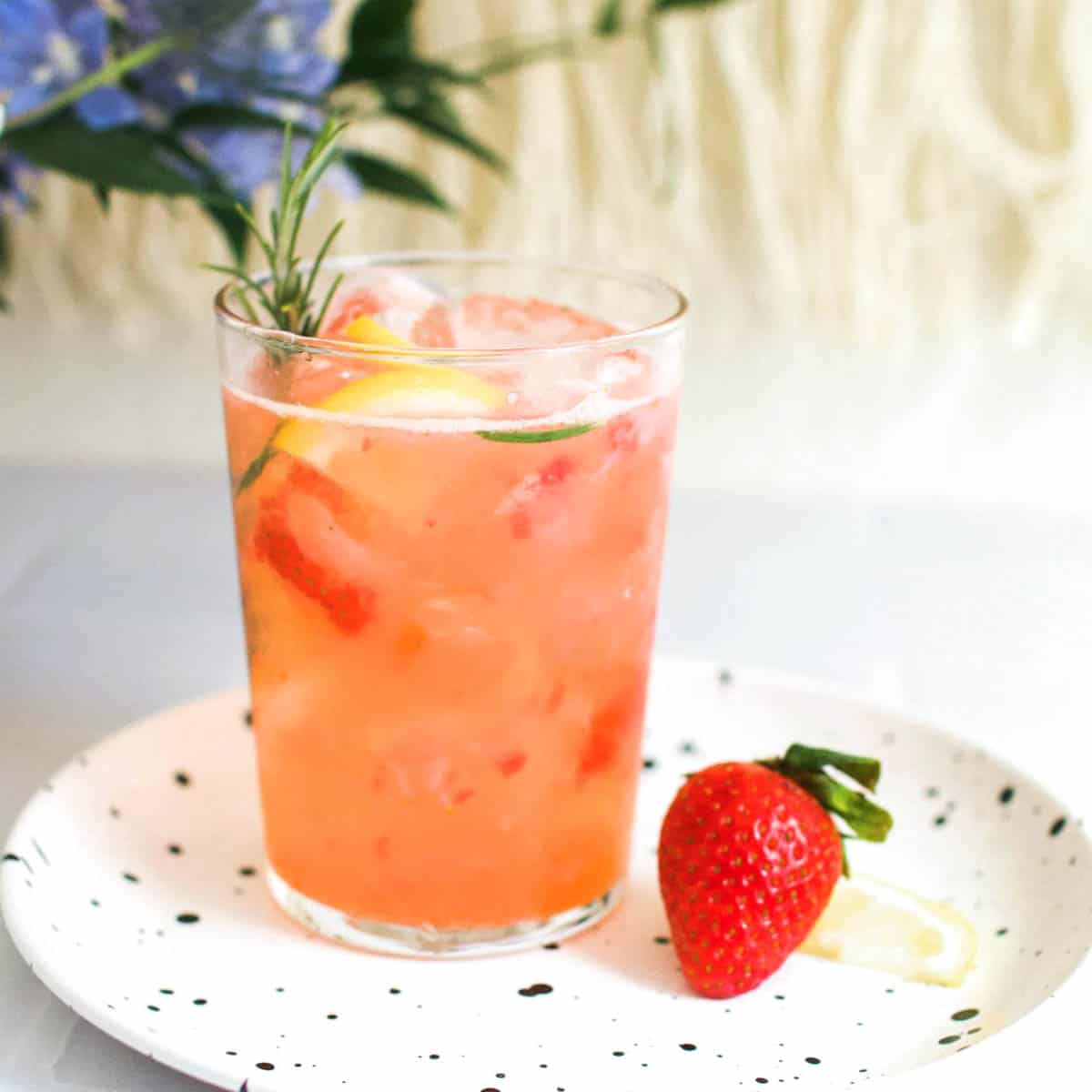 Strawberry mocktail on a little tray on a table with a strawberry next to the glass.